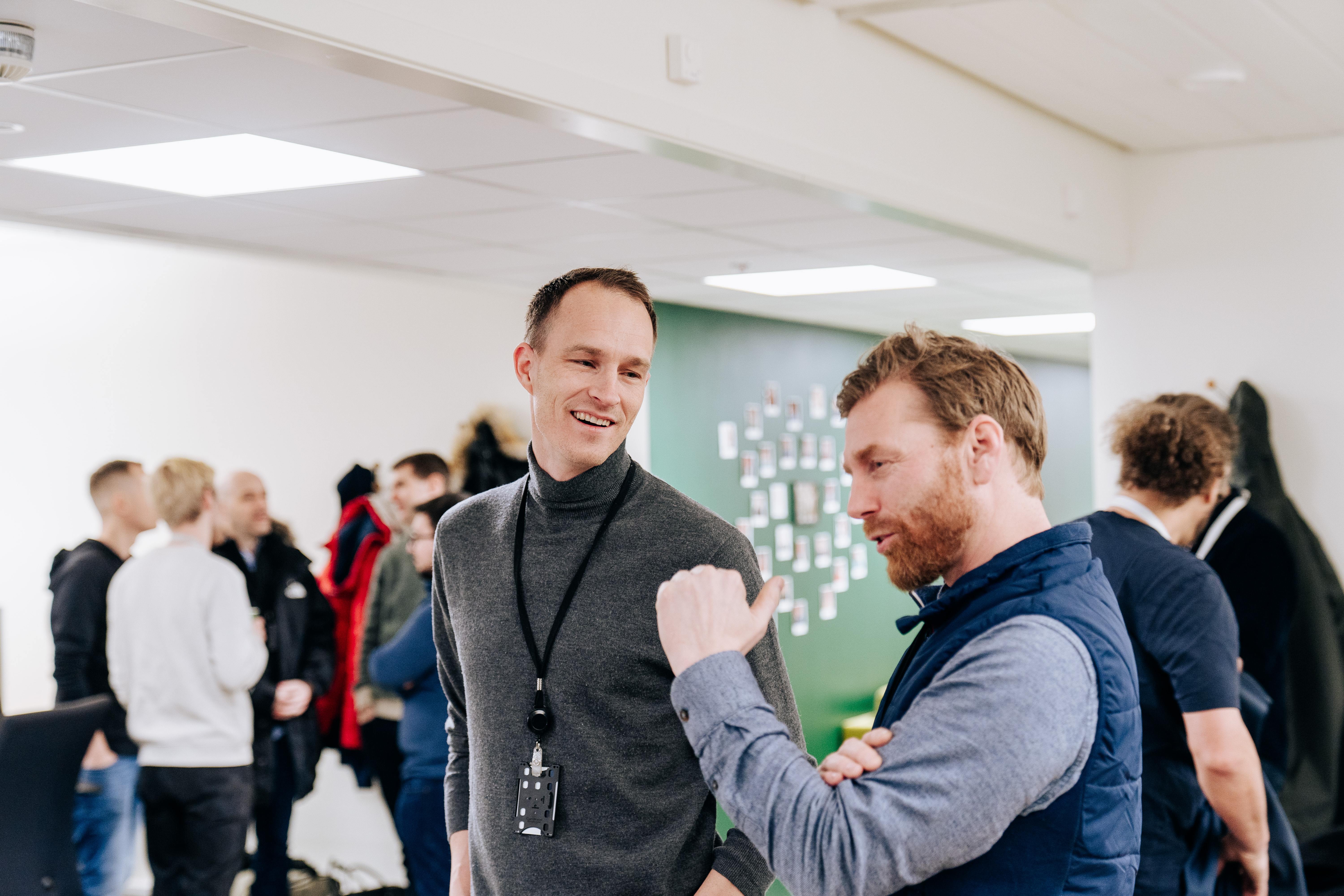 Two Catenda team members laughing and talking in an office with a green accent wall covered in sticky notes