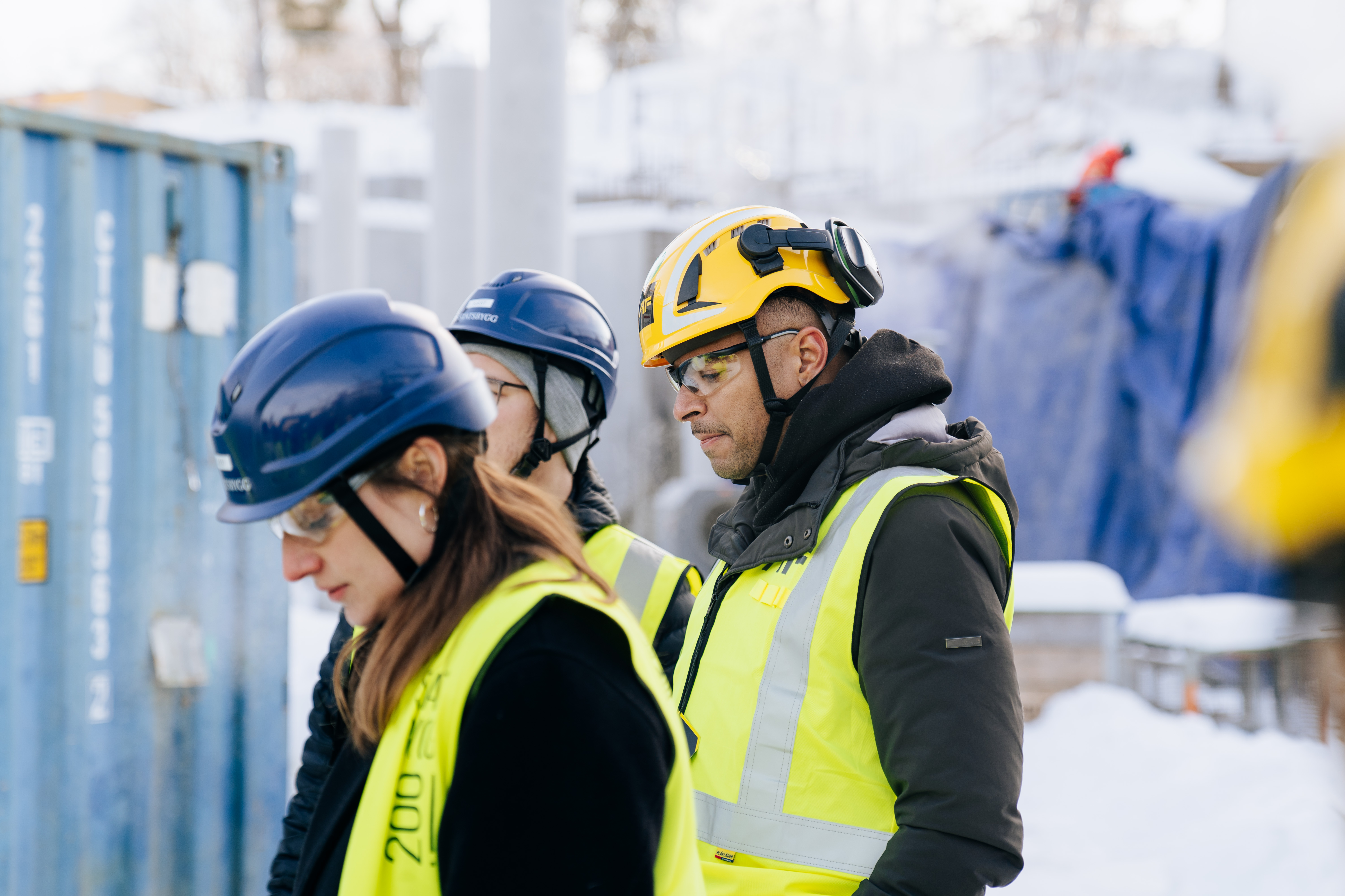 Three Catenda team members in yellow hi-vis vests and hard hats at a snowy construction site
