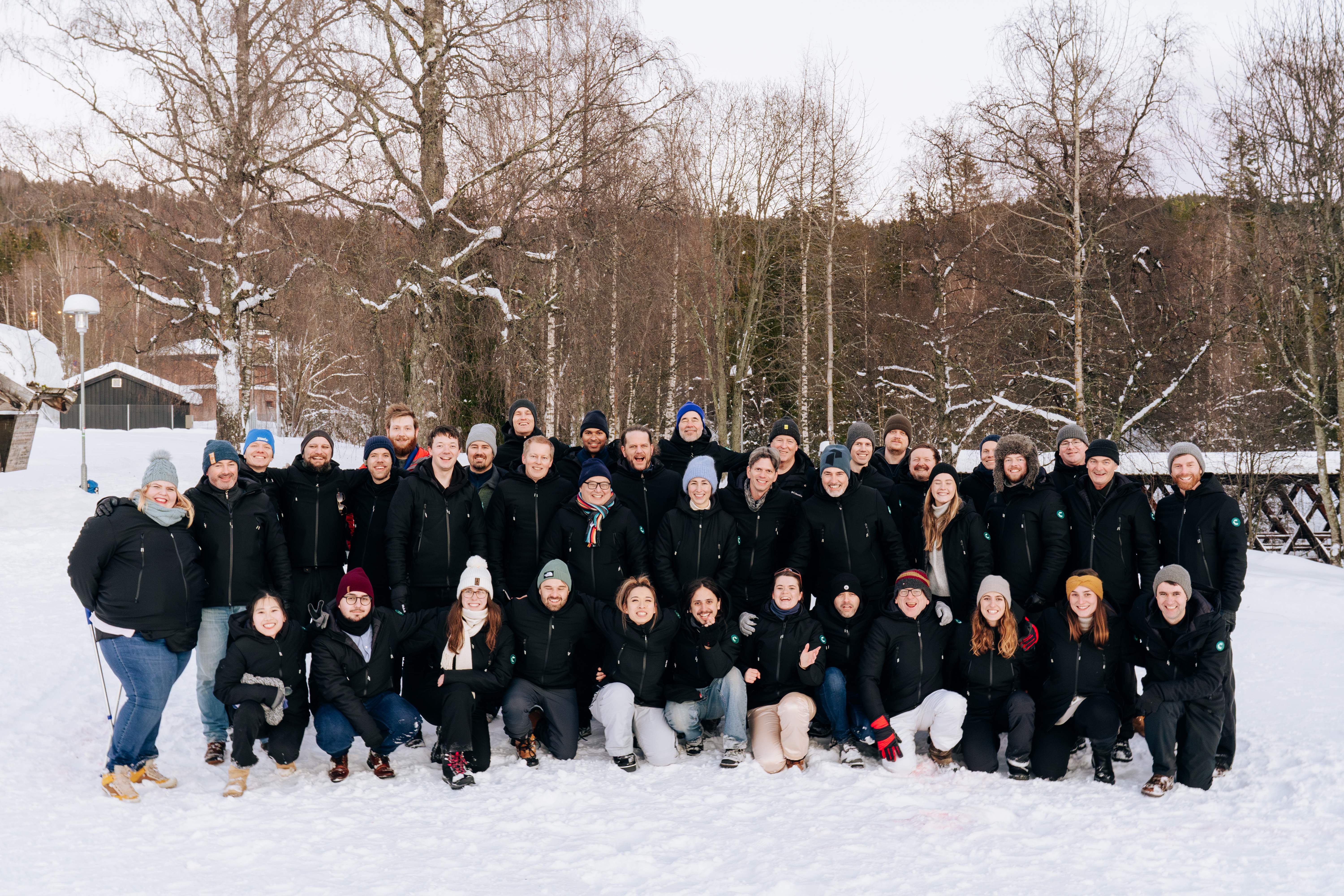 The full Catenda team gathered outdoors in a snowy birch forest, wearing matching black jackets and colourful winter hats