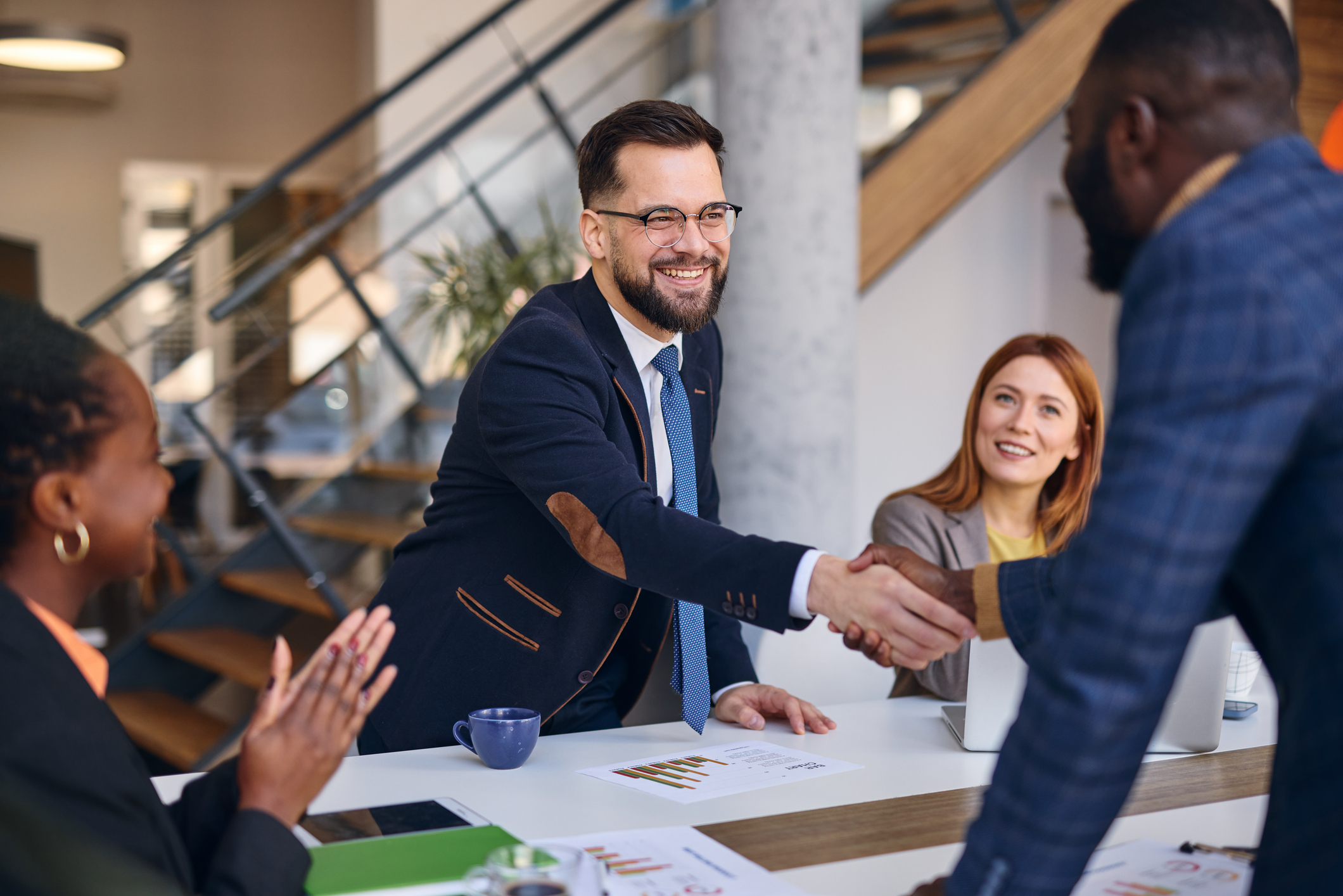 Two partners shaking hands across a table during a meeting in a bright modern office