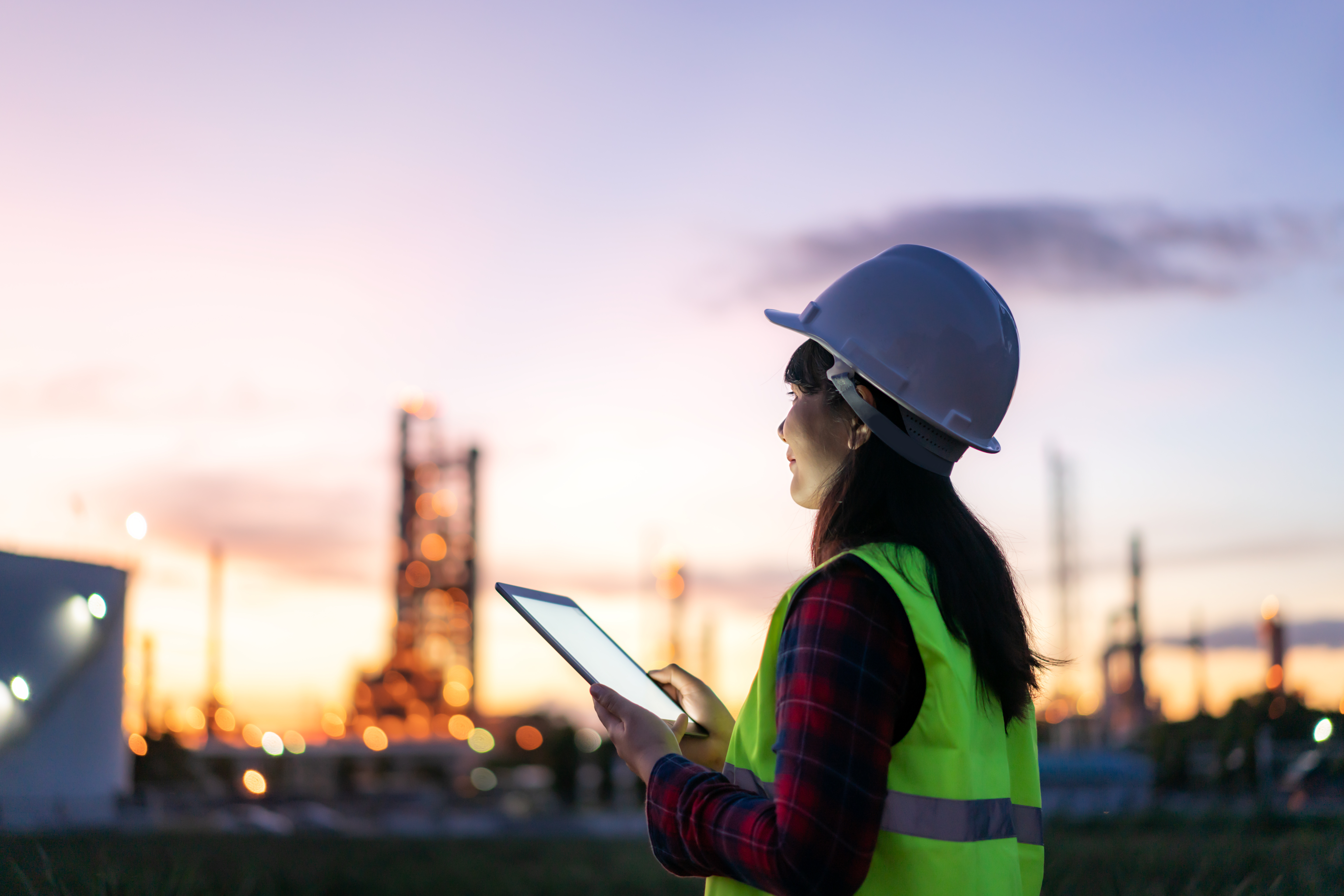 Asian woman engineer working at night with digital tablet Inside an oil and gas refinery plant construction for inspector safety quality control