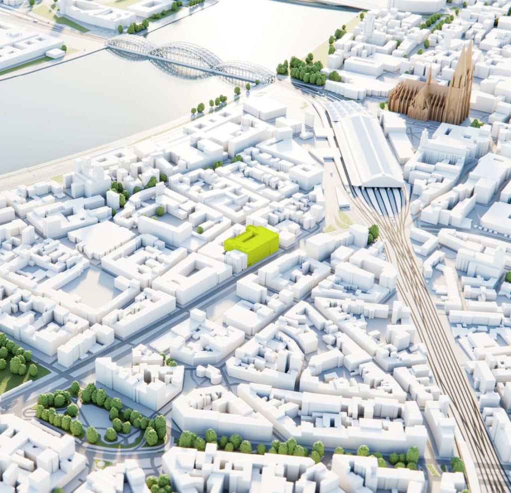 3D white-box city model of Cologne, highlighting the MACO building site in bright green near the Rhine River and main station.